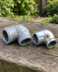 Hot-dip galvanised pipe elbow next to a zinc-plated elbow with surface rust