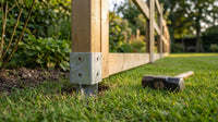 Galvanised fence post spike driven flush into a lawn beside a part-built timber fence, sledgehammer resting on the grass