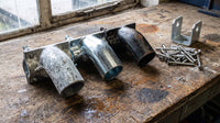 Steel tube fittings in three finishes: matte grey hot-dip galvanised, bright electroplated zinc and bare black steel, beside a galvanised post support bracket and stainless steel screws