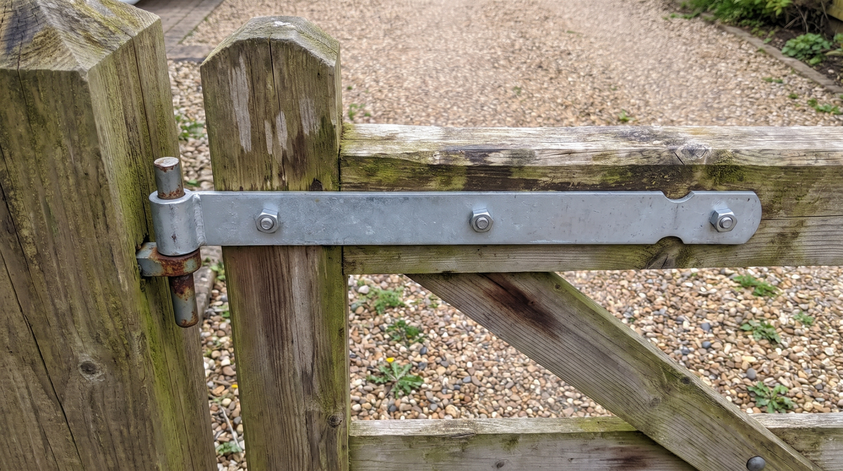 Zinc-plated gate band hinge bolted across the top rail of a wooden gate, hung on a pin at the gate post