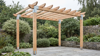 Timber pergola with galvanised steel corner connectors at the post tops and bolt-down post shoes at the base, on a paved garden patio.