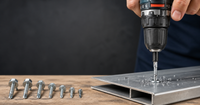 how to use self drilling screw: person uses a power drill to drive a self-tapping metal screw into a steel channel while various sizes of screws sit on a wooden surface.