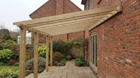 Wall-mounted lean-to timber pergola fixed to a red brick house wall with galvanised steel brackets, posts standing on the paved terrace